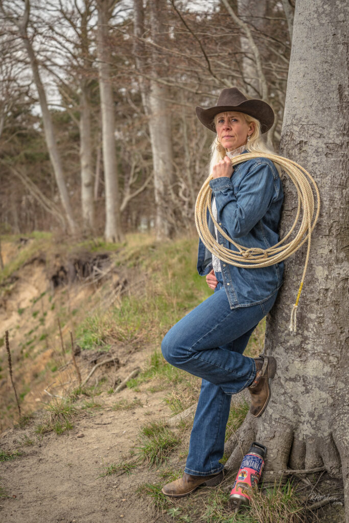 Dea Larsen ved kysten med cowboyhat og reb over skulderen. Kendt fra Alene i Vildmarken sæson 10 på DR, hvor natur, eventyr og personlig udvikling er centrale temaer.