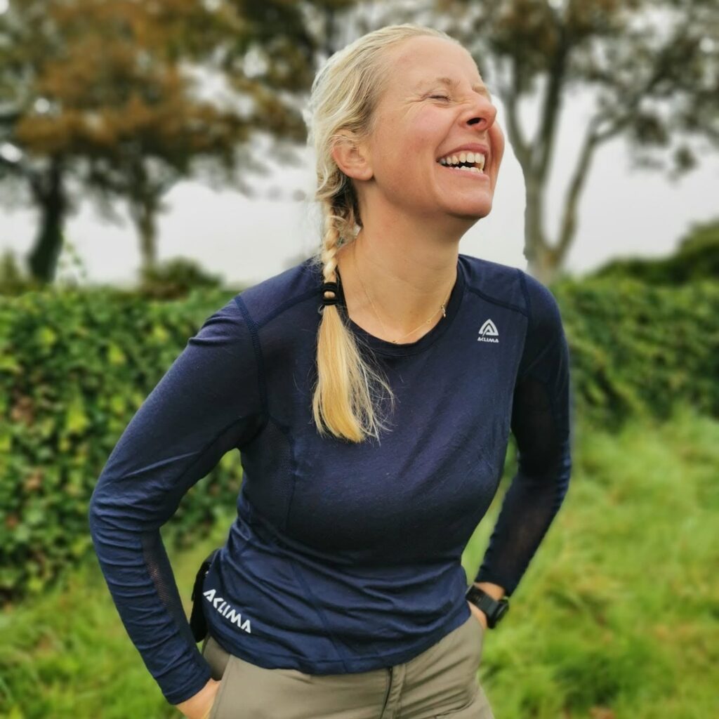Smilende Dea Larsen med et stort grin. Billedet understøtter den humoristiske fortælling om de spørgsmål, hun oftest får efter Alene i Vildmarken.