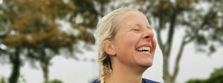 Smilende Dea Larsen med et stort grin. Billedet understøtter den humoristiske fortælling om de spørgsmål, hun oftest får efter Alene i Vildmarken.