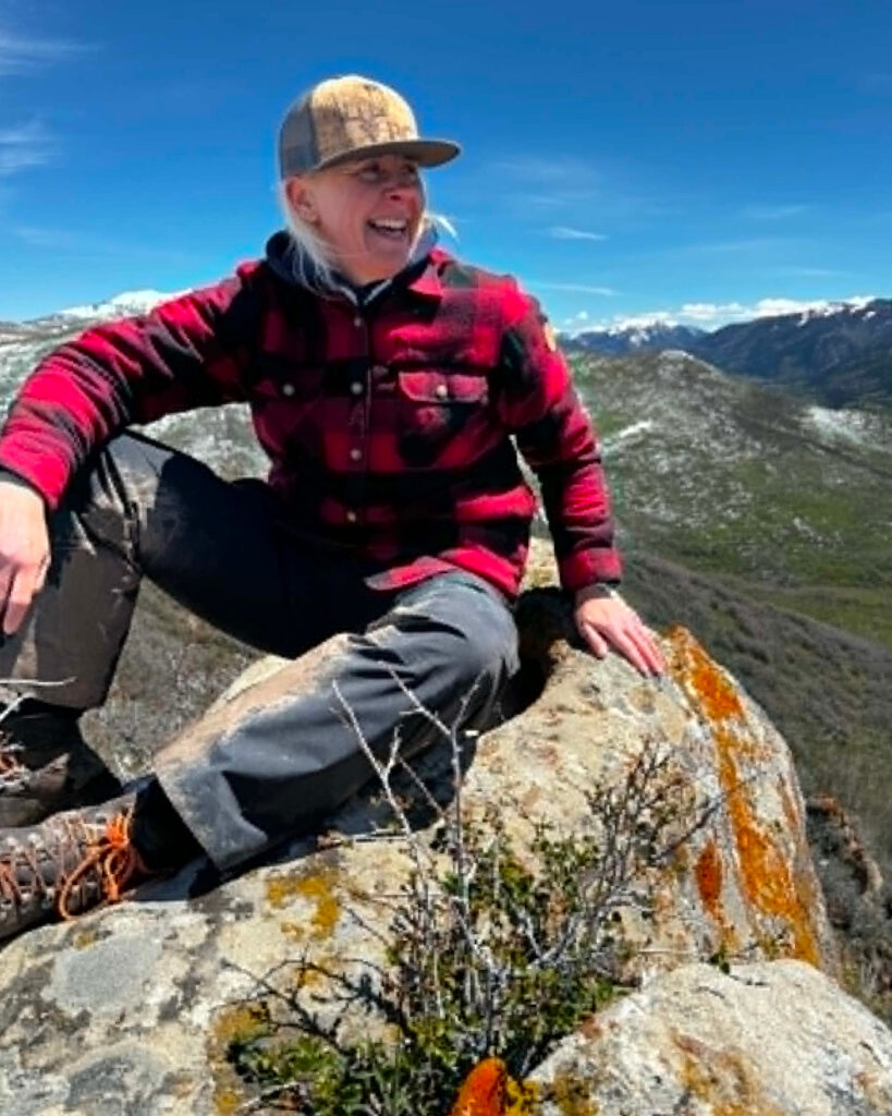 Dea Larsen siddende på en klippe i bjerglandskab. Kendt fra Alene i Vildmarken sæson 10, outdoor-entusiast, lystfisker og indehaver af Outdoor i Centrum.